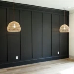 An empty room with a black, paneled wall, two hanging rattan pendant lights, light wood flooring, and two electrical outlets on the wall.