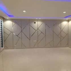 A modern empty room featuring a tiled floor, geometric patterned wall, recessed ceiling lights, and blue LED strip lighting along the ceiling perimeter.